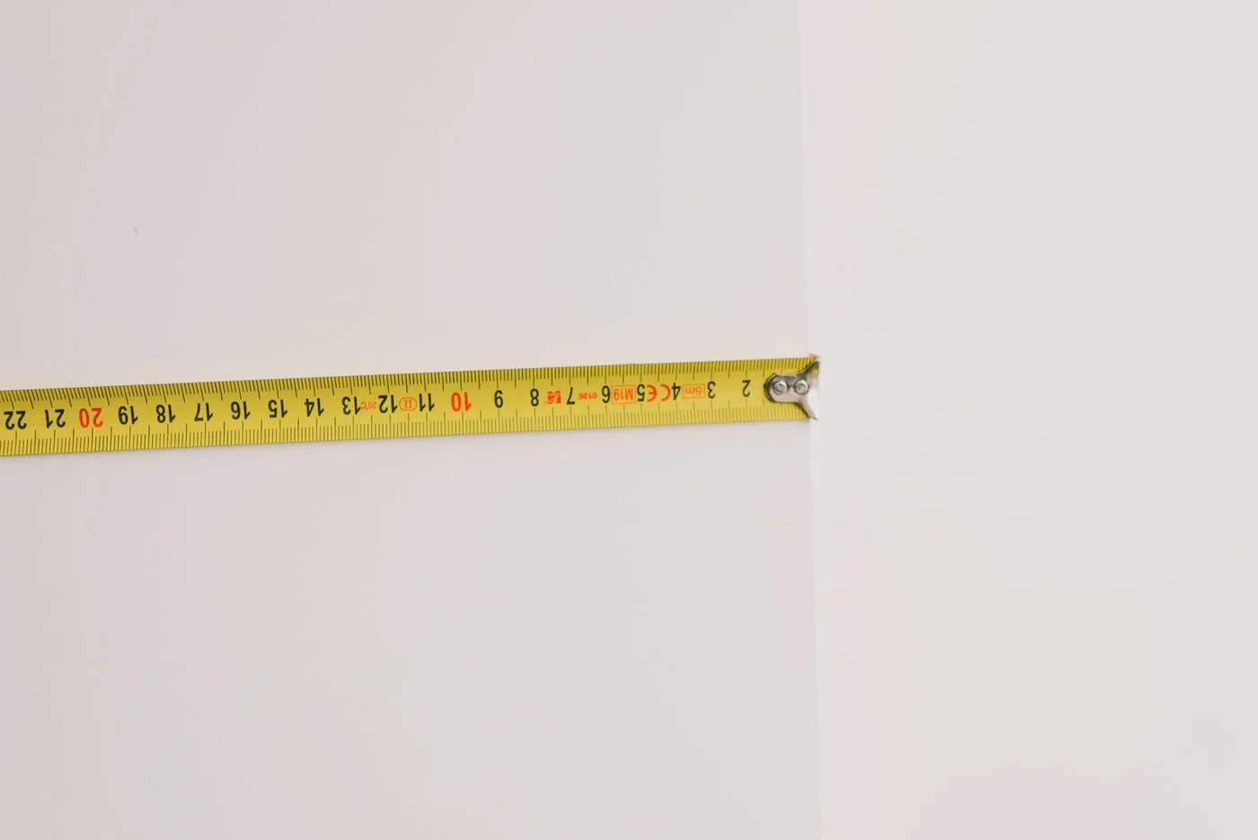 白い壁に沿わせて伸ばした、目盛りの見える黄色いメジャー